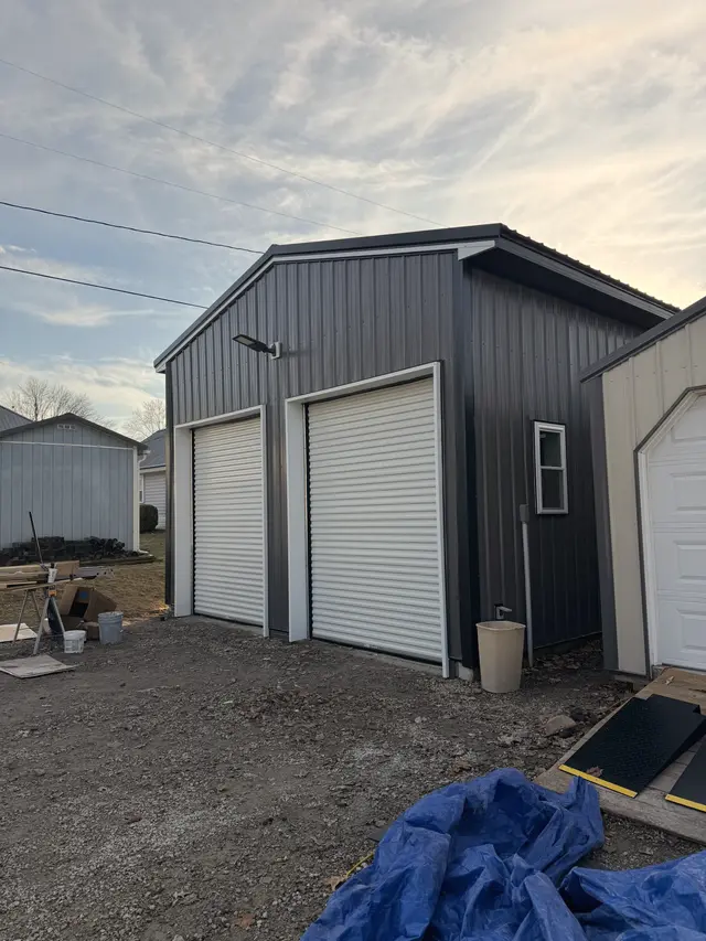 A finished black metal barn with white roll-up doors.