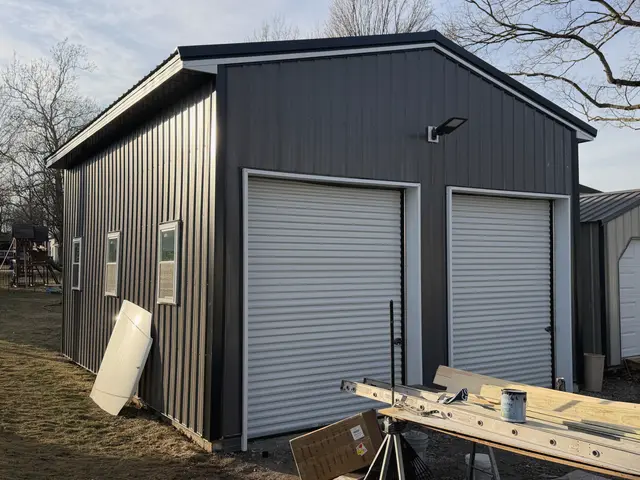 The exterior of a black metal barn with white roll-up doors.