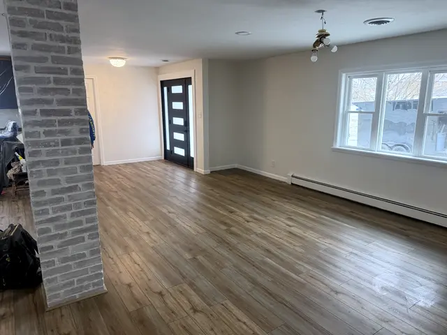A finished room with wood floors, a brick column and a black door.