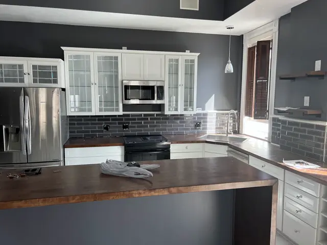 A kitchen remodeled by ZKB: white glass-front cabinets, a dark tile backsplash and a wood-top island.