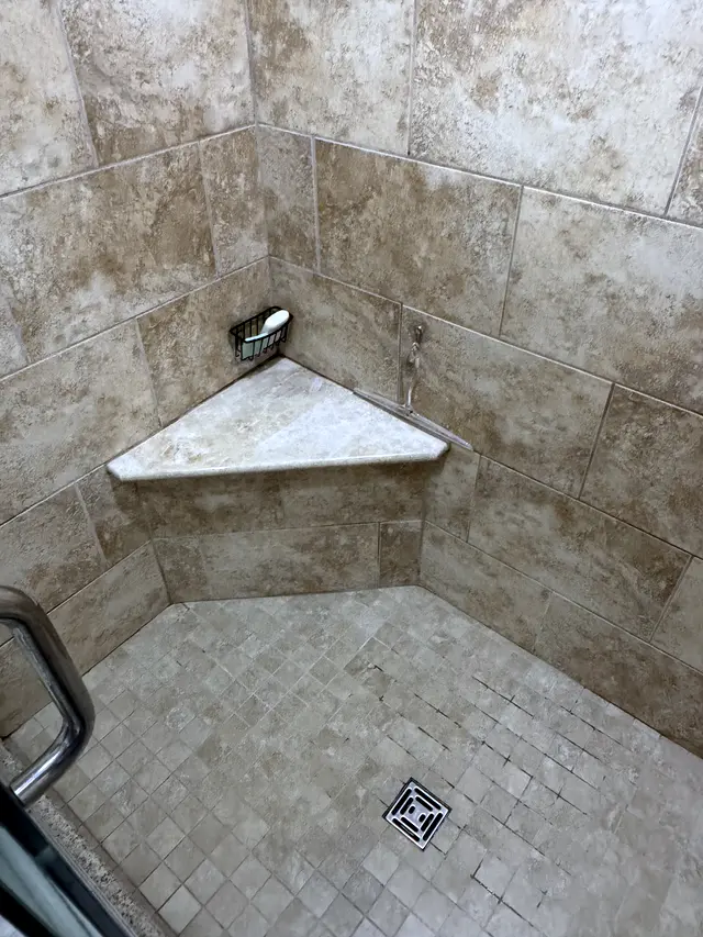 A finished walk-in shower tiled floor to ceiling, with a built-in corner shelf.